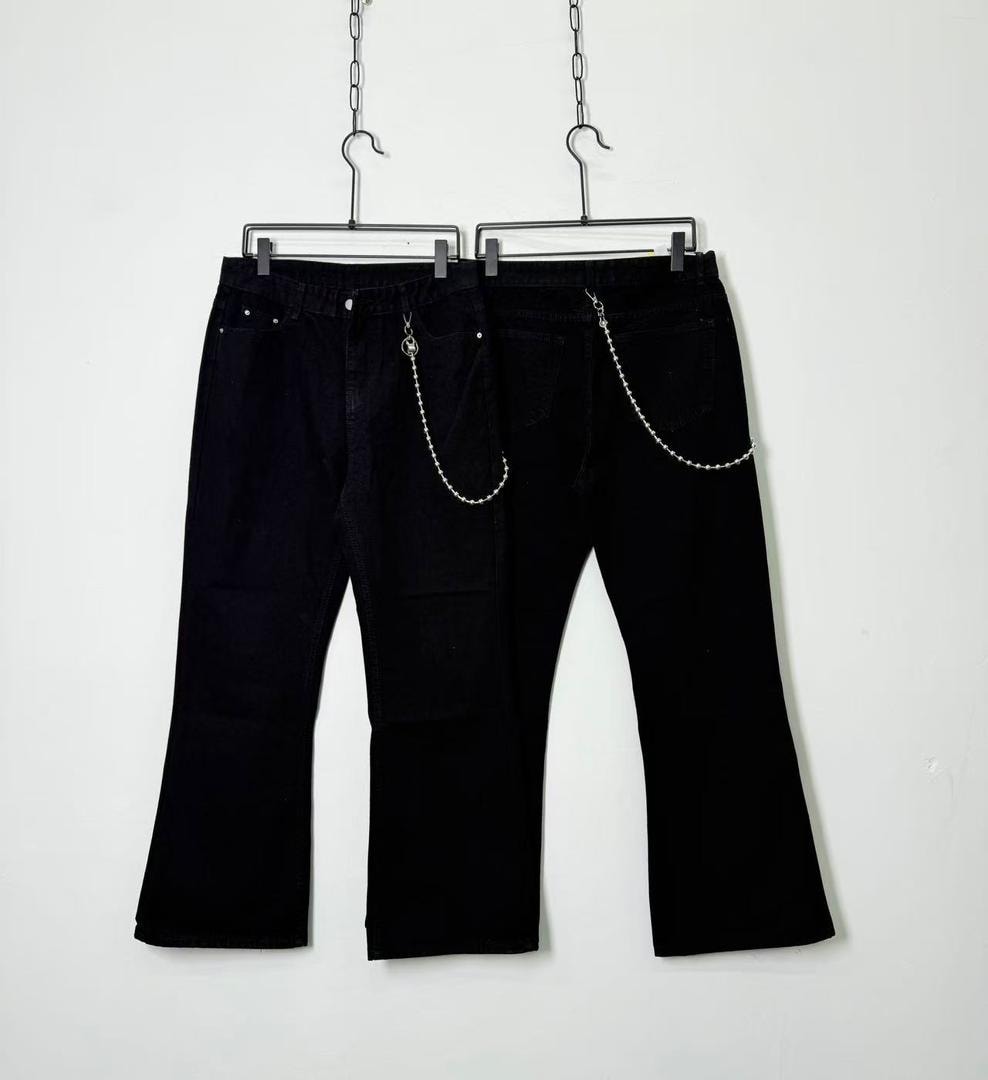 Two pairs of black baggy jeans with silver chain details hanging against white background.