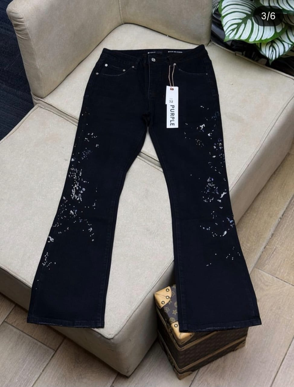 Black splatter flared jeans laid flat on a beige couch with visible tag and plant in background.
