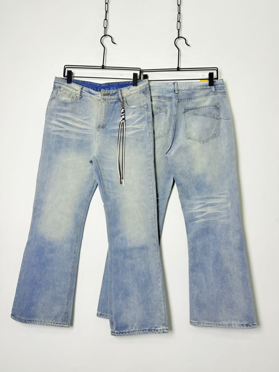 Front and back views of light blue flared jeans with drawstring detail hanging on black hangers.