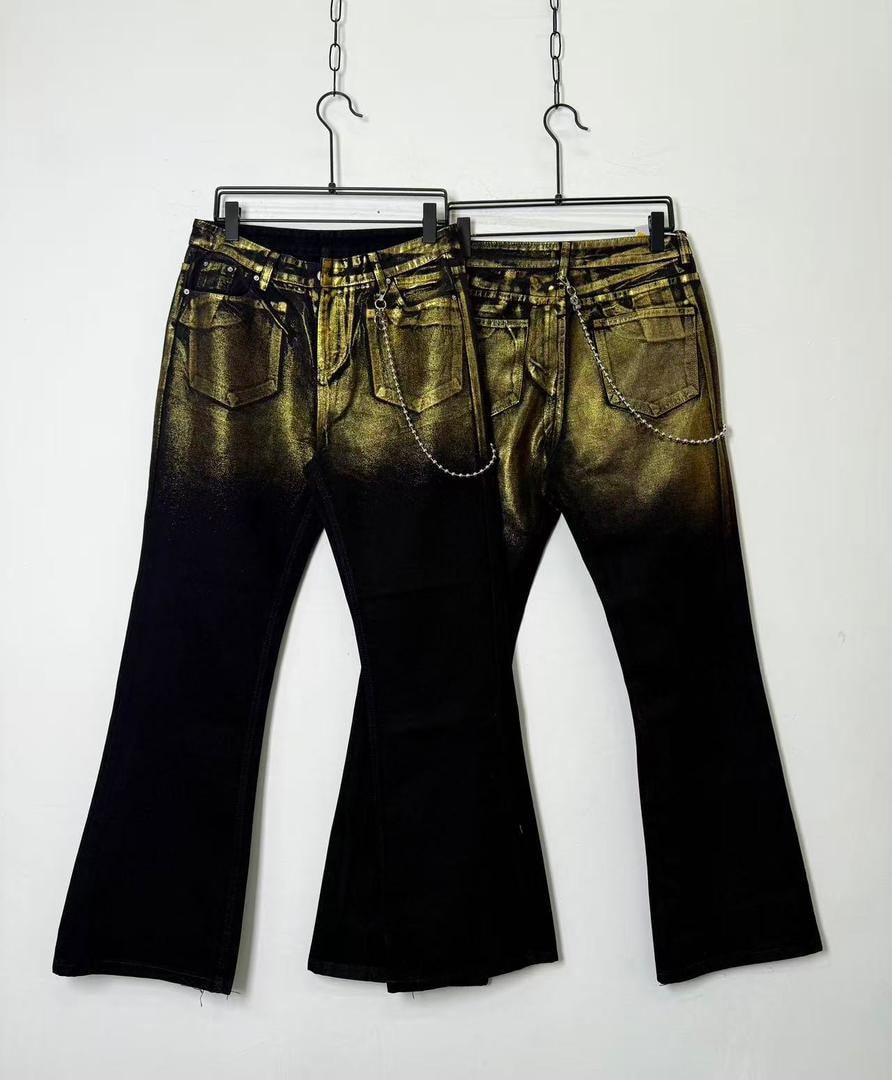 Two pairs of black and gold ombre flared jeans with chain details shown from the back on hangers.