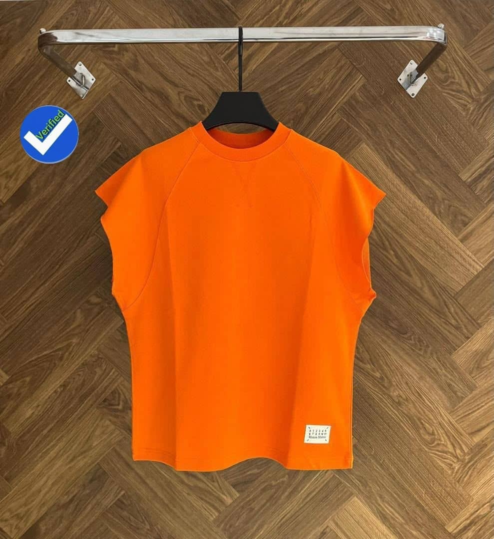 Bright orange armless raglan top on black hanger against wooden floor.