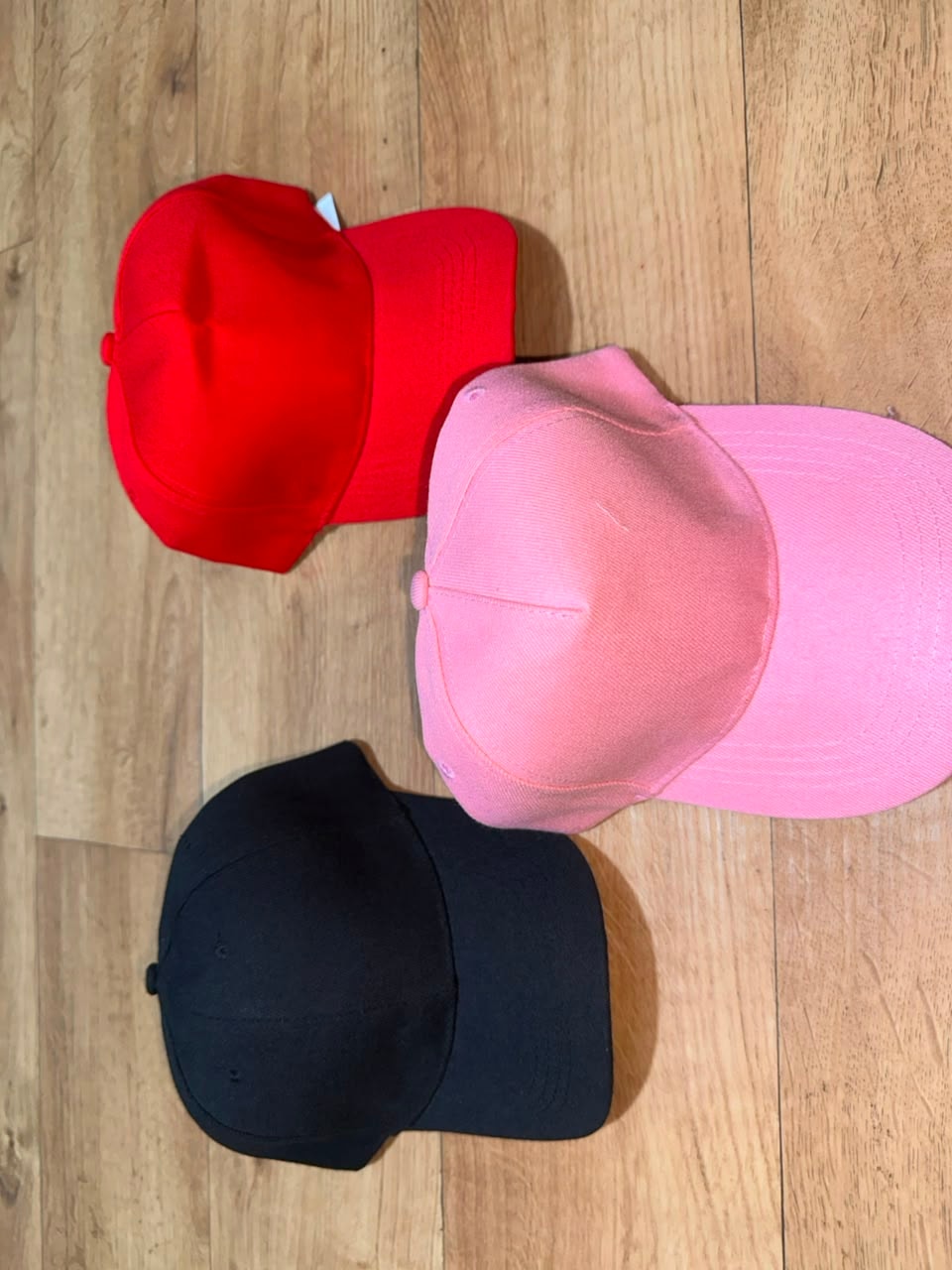 Plain baseball caps in red, pink, and black colors.