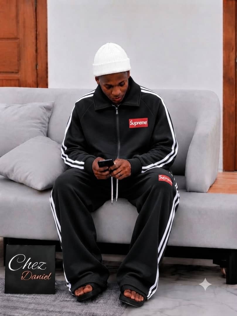 Model wearing black Supreme zip-up tracksuit with white stripes.