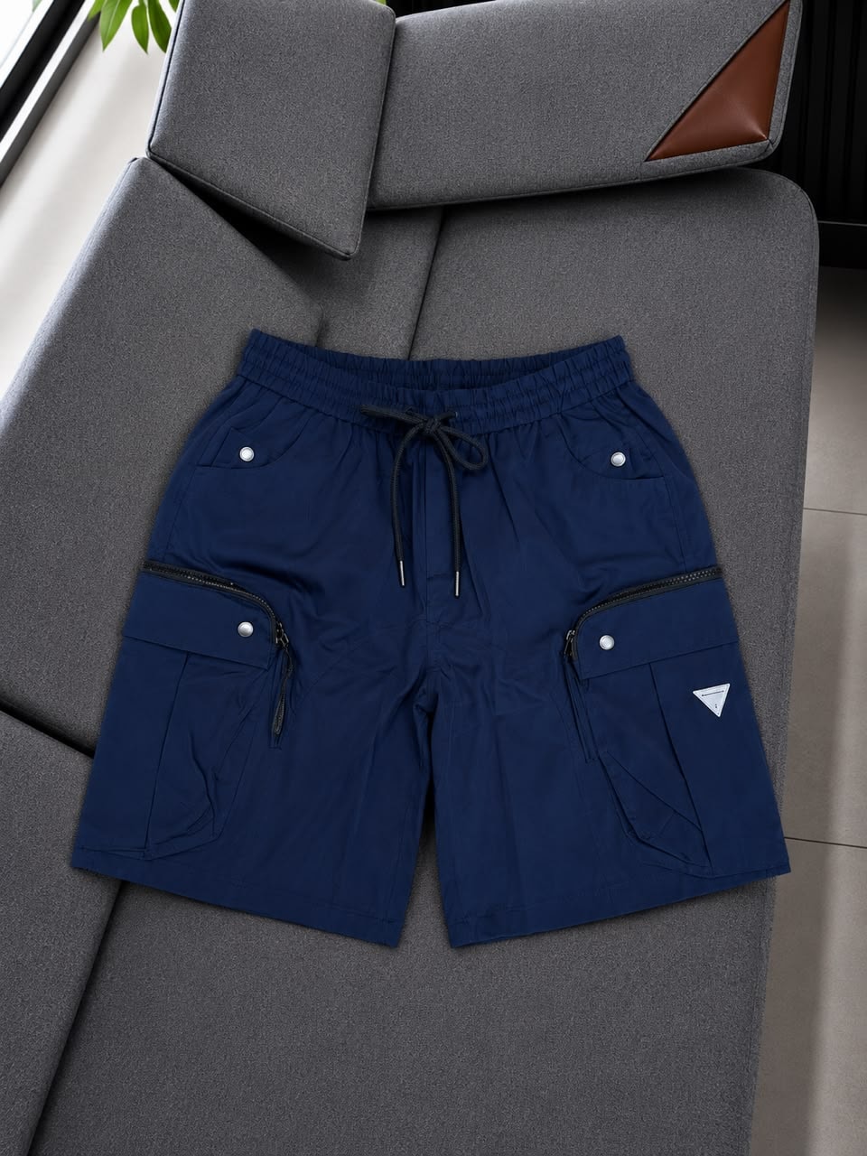 Navy cargo shorts with triangle logo displayed on sofa.